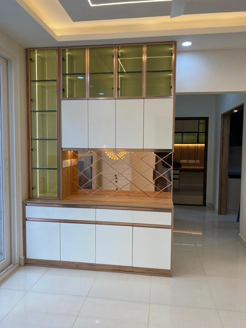 Custom white and wood storage with illuminated glass cabinets and a mirror backsplash